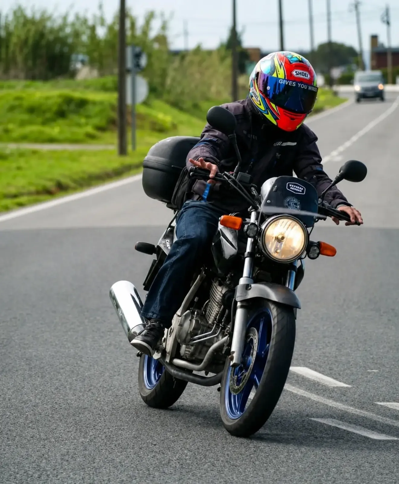 Motociclista de capacete Shoei numa Honda CB 250 clássica, numa estrada do interior